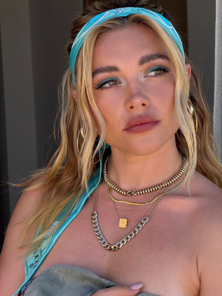 Florence Pugh posing in a blue head scarf and gold necklaces